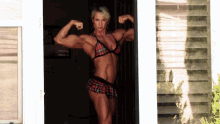a woman in a plaid bikini is flexing her muscles in front of a window