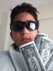 a young boy wearing sunglasses and holding a bunch of one dollar bills