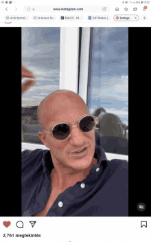 a bald man wearing round sunglasses is sitting in front of a window on instagram