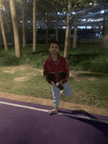 a young boy in a red jacket stands on one leg on a purple road