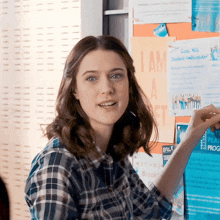 a woman in a plaid shirt is pointing at a poster that says i am a student ambassador