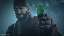 a man with a beard is holding a green bottle in his hand in the dark .