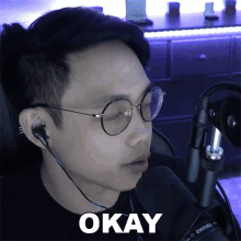 a man wearing glasses and earbuds says okay in front of a microphone