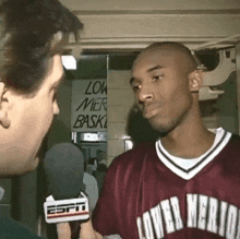 a man wearing a lower merlot jersey is talking into a microphone