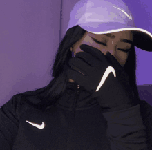 a woman wearing a nike hat covering her face with her hand