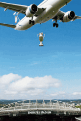 a plane is flying over emirates stadium with a trophy hanging from the wing