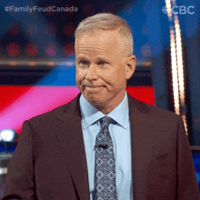 a man in a suit and tie is standing in front of a microphone with the words family feud canada behind him