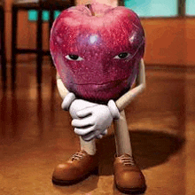 a red apple with arms and legs is sitting on the floor .