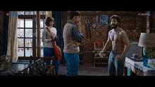 a man without a shirt is standing in a living room talking to two other men