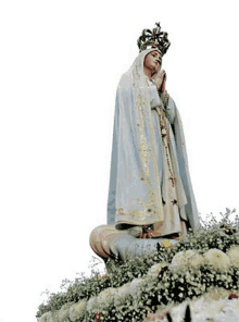 a statue of the virgin mary with a crown on her head is surrounded by flowers and a rosary .