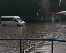 a white van is driving through a flooded street near a deluxe sign