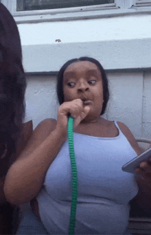 a woman in a white tank top is smoking a hookah while holding a cell phone