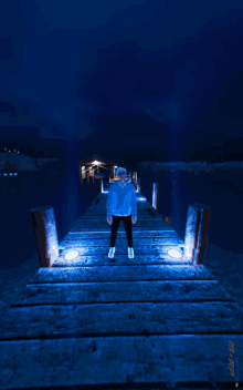 a man in a blue sweater is standing on a wooden pier