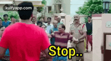 a man in a red shirt is standing in front of a crowd of people while a police officer stands behind him .