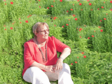 a woman in a red shirt and white pants sits in a field of flowers