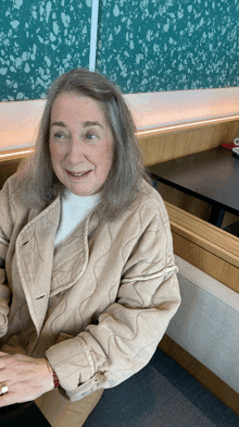 a woman wearing a tan jacket and a white sweater sits at a table