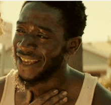 a man in a white tank top is smiling and holding his hand to his chest