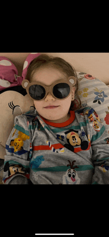 a little girl wearing sunglasses is laying on a pillow