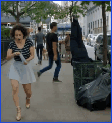 a woman is running towards a trash can with a man hanging upside down in it