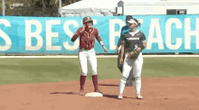 two women are standing on a baseball field in front of a banner that says ' s best peach ' .