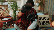 a woman wearing boxing gloves is sitting on a yoga mat in front of a pillow that says good vibes