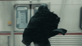 a woman in a black coat is standing in front of a subway car