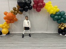 a little girl stands in front of a wall covered in balloons