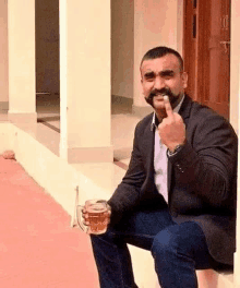 a man with a mustache is sitting on a porch holding a beer mug and giving the middle finger .