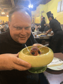 a man in a black shirt is holding a bowl of food with a straw in it