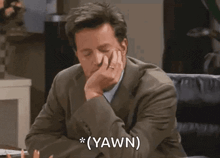 a man in a suit and tie is sitting at a desk with his hand on his chin and says `` yawn '' .