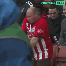 a man in a red and white striped shirt is standing in a stadium with the words football daily on the bottom