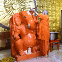 a statue of an elephant is being cleaned by a man in an orange robe