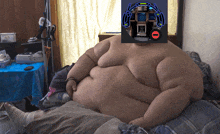 a very fat man laying on a bed with a picture of a robot on his face