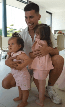 a man is kneeling down holding two little girls in his lap