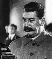 a black and white photo of a man with a mustache looking at a cell phone .