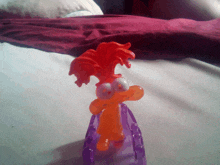 a toy with orange hair and big eyes is sitting on a purple object