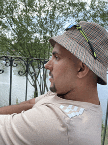 a man wearing a bucket hat and sunglasses sits on a balcony overlooking a body of water