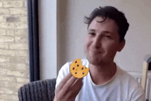 a man in a white shirt is holding a cookie in front of his face