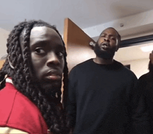 two men with dreadlocks and a beard are standing next to each other in front of a door .