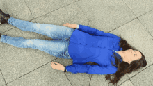 a woman in a blue shirt and jeans is laying on the ground with her eyes closed