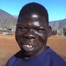 a man in a blue shirt is smiling with mountains in the background .