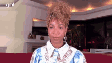 a woman with curly hair is sitting on a red couch in a living room looking at the camera .