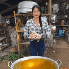 a woman in a plaid shirt is holding a tray of food in front of a large pot of soup