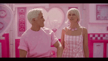 a man and a woman are standing in a pink room with a sign that says ' barbie ' on it