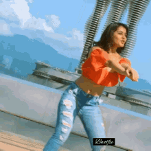 a woman in a red top and jeans is dancing on a rooftop .