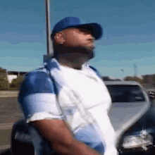 a man wearing a blue hat and a white shirt is standing next to a car in a parking lot .