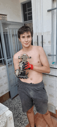 a shirtless man wearing a pair of red gloves is holding a piece of metal