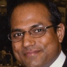 a close up of a man wearing glasses and a suit and smiling .