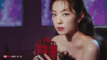 a woman is holding a red gift box with a red ribbon .