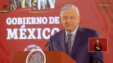 a man in a suit and tie stands at a podium in front of a sign that says gobierno de mexico